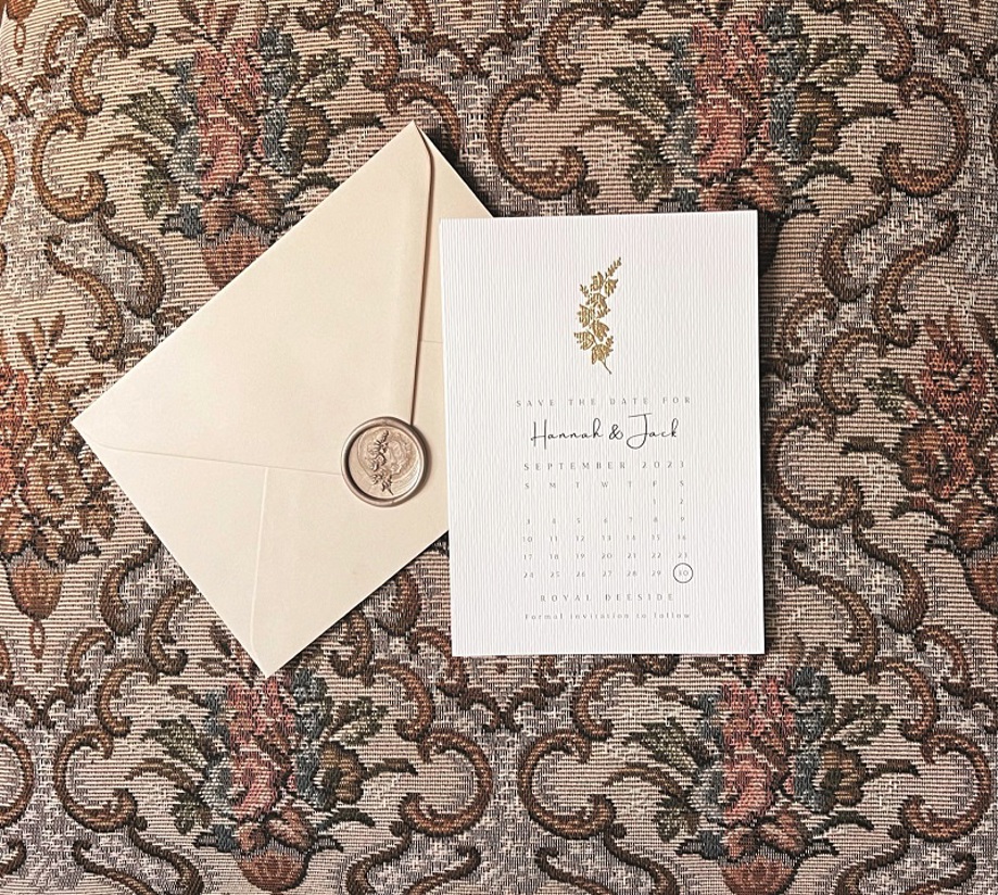 White save the date with gold embossed sprig of heather and cream envelope with wax seal and sprig of heather